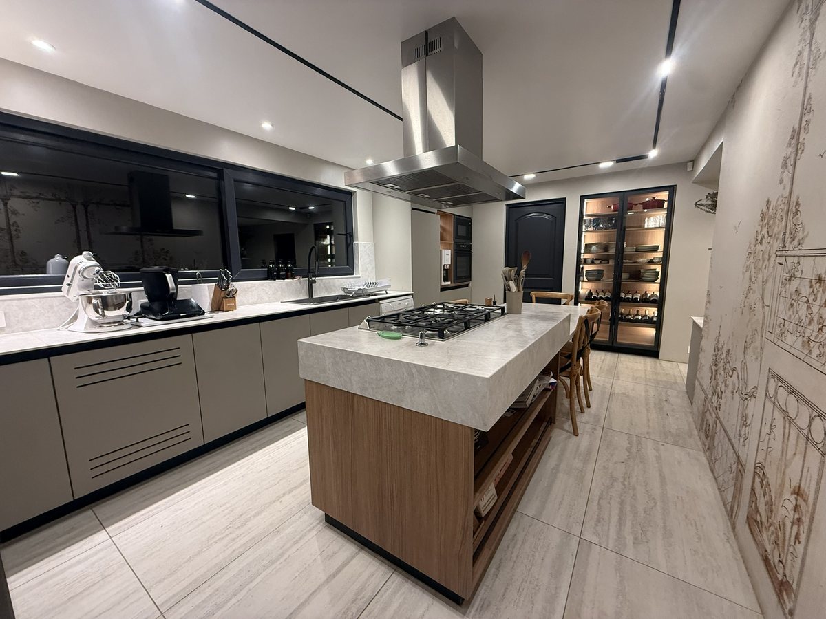Cocina remodelada con isla de madera y cubierta de piedra, campana de acero y vitrina iluminada